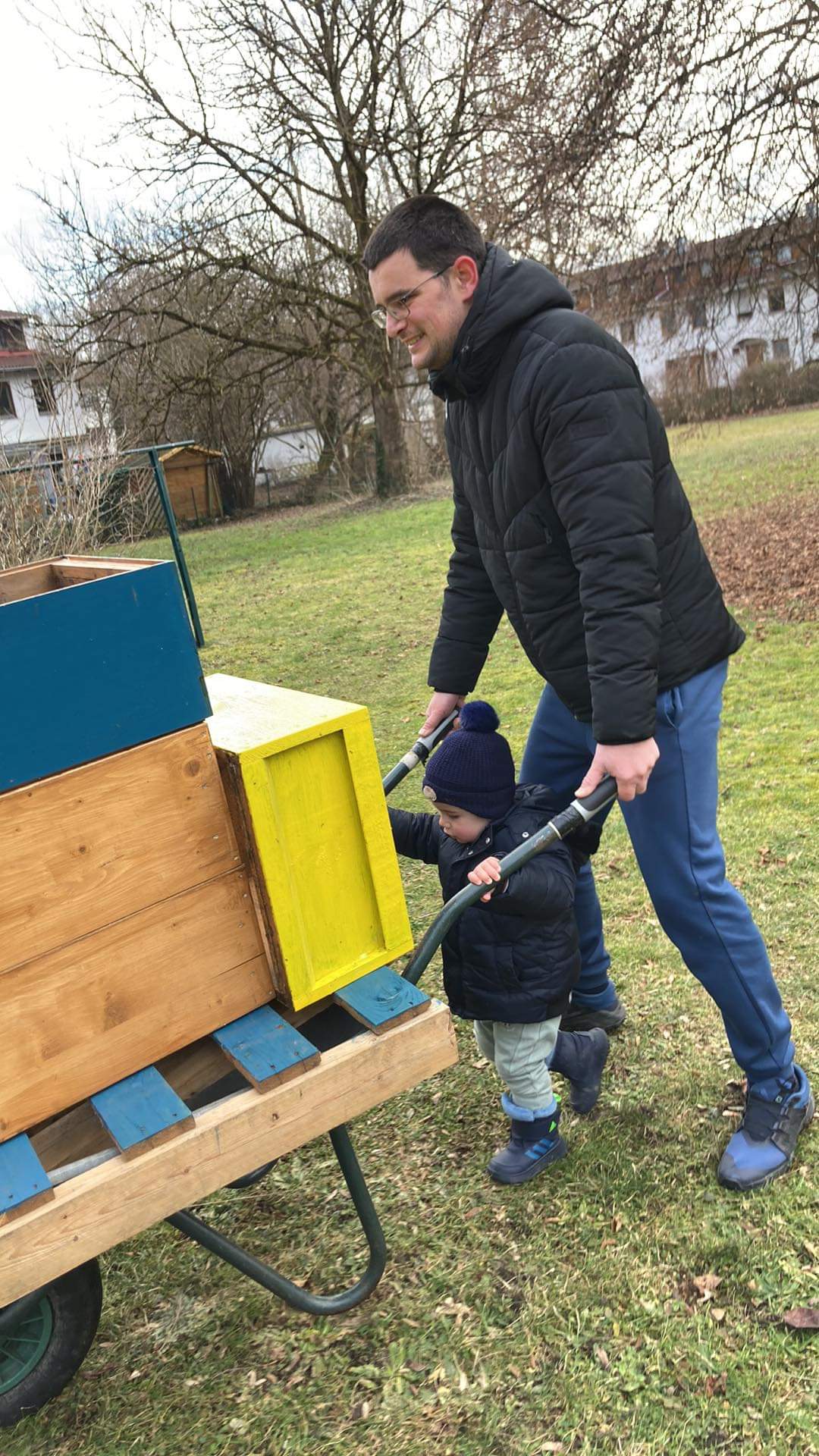 Father and toddler carrying beehive boxes together during family beekeeping